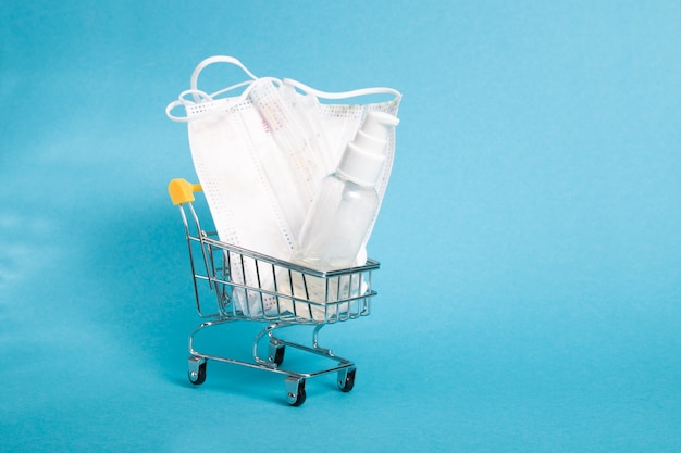 Máscaras de proteção facial e gel desinfetante no carrinho de compras, fundo azul, espaço de cópia