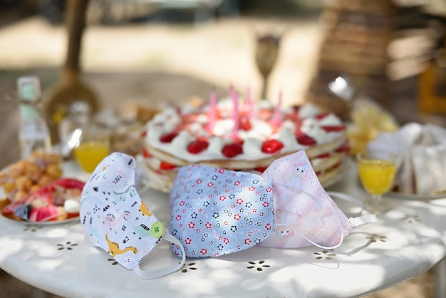 Máscaras de proteção para crianças na mesa de aniversário com bolo e doces