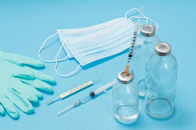 Máscaras médicas luvas garrafas de vidro para medicamentos líquidos e seringas para injeção em fundo azul