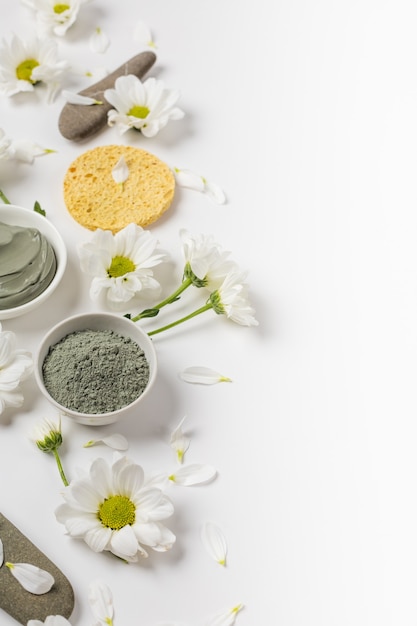 Mascarilla de arcilla natural seca y húmeda con flores sobre un fondo blanco.