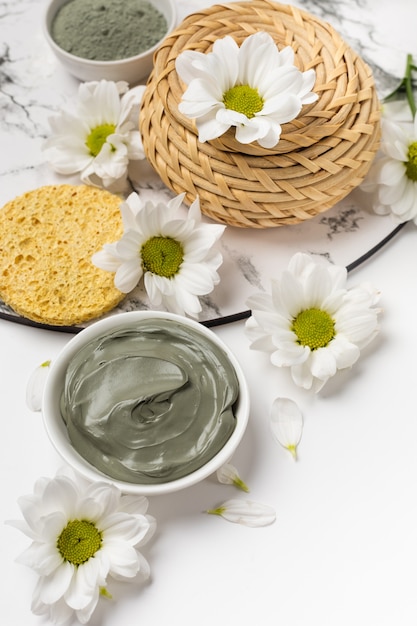 Mascarilla de arcilla natural seca y húmeda con flores sobre un fondo blanco.