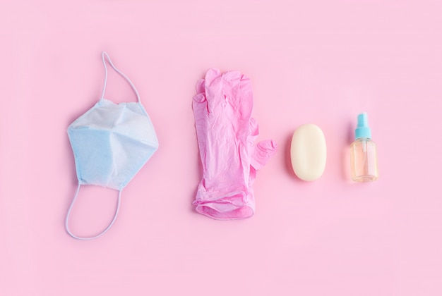 Foto la mascarilla azul, los guantes rosados y el aptico de la mano mienten en un fondo rosado.