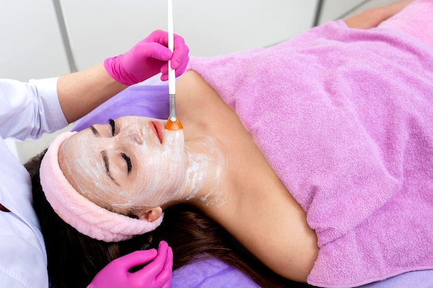 Mascarilla exfoliante facial, tratamiento de belleza spa, cuidado de la piel. Mujer recibiendo cuidado facial por esteticista en el salón de spa, vista lateral, primer plano. Tratamiento anti-envejecimiento. Cosmetología y cuidado de la piel facial profesional.