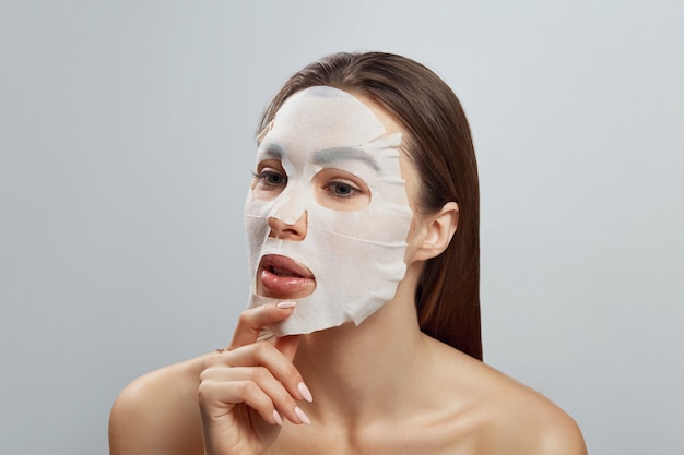 Mascarilla facial de belleza. Hermosa mujer con una máscara hidratante de tela en la cara.Cuidado de la piel.Modelo de belleza chica toca su rostro. máscara de spa.