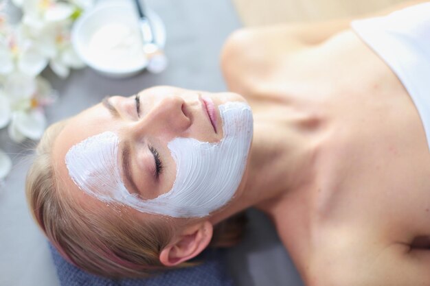 Mascarilla hermosa niña en spa esteticista mujer aplicando mascarilla facial