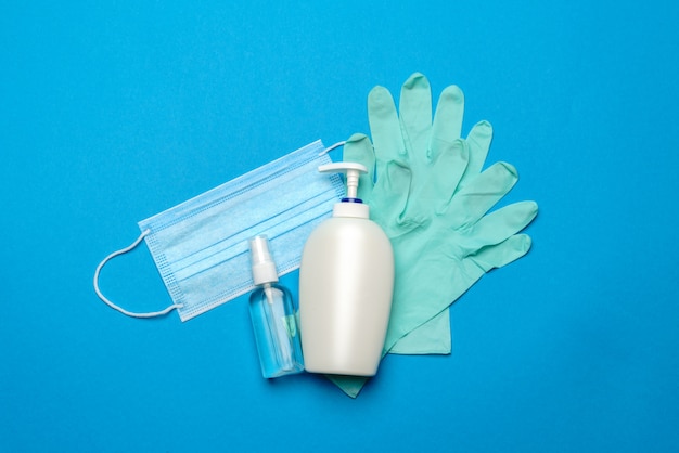 Mascarilla médica azul desechable, guantes de látex de goma y antiséptico desinfectante de manos con alcohol en la pared azul