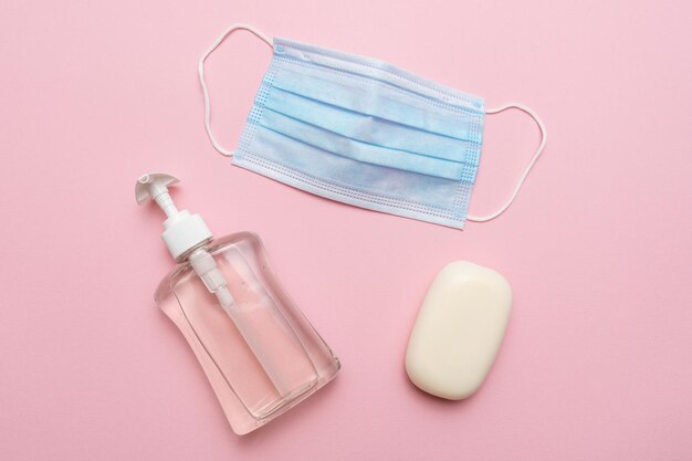 Mascarilla médica azul, jabón y jabón fluido sobre fondo rosa. Concepto de protección contra la pandemia del virus de la corona covid 19.