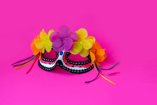 Mascarilla mexicana con flores y cintas en el fondo rosa. Concepto del día de los muertos