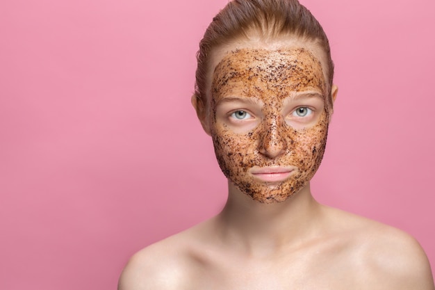 Mascarilla de posos de café exfoliante facial para la piel en el rostro de una hermosa mujer joven