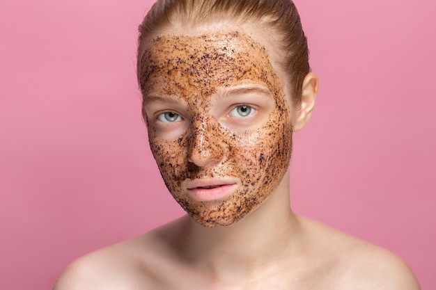 Mascarilla de posos de café exfoliante facial para la piel en el rostro de una hermosa mujer joven