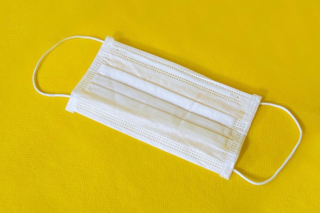 Mascarilla quirúrgica con correas de goma para los oídos Mascarilla quirúrgica típica de 3 capas para cubrir la boca y la nariz sobre fondo amarillo