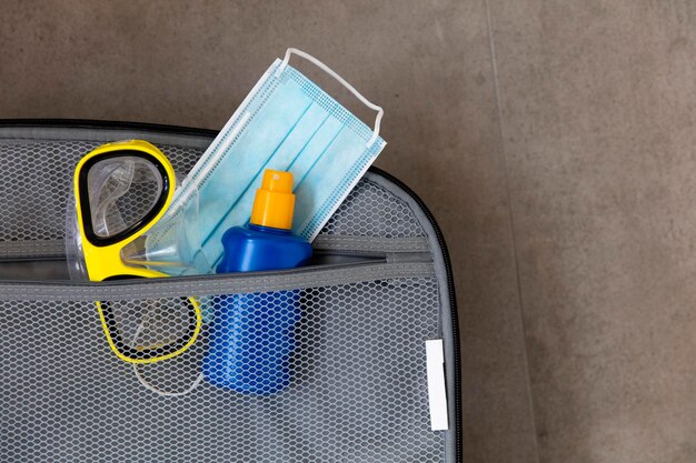 Mascarilla quirúrgica protectora crema solar y máscara de buceo en una maleta de viaje
