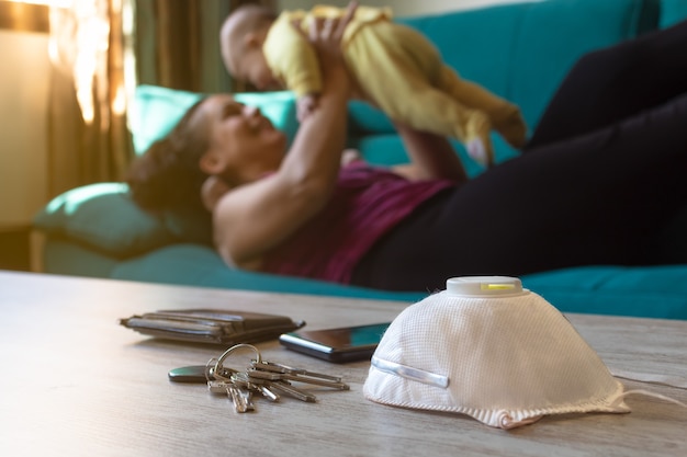 Mascarilla sobre la mesa y mujer sosteniendo a un bebé