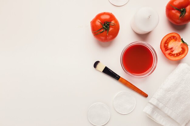 Mascarilla de tomate para el cuidado de la belleza natural. Tarro de pasta jugosa, vegetales frescos rojos, cepillo aplicador sobre fondo blanco, concepto de spa y cosmética casera, espacio de copia, vista superior