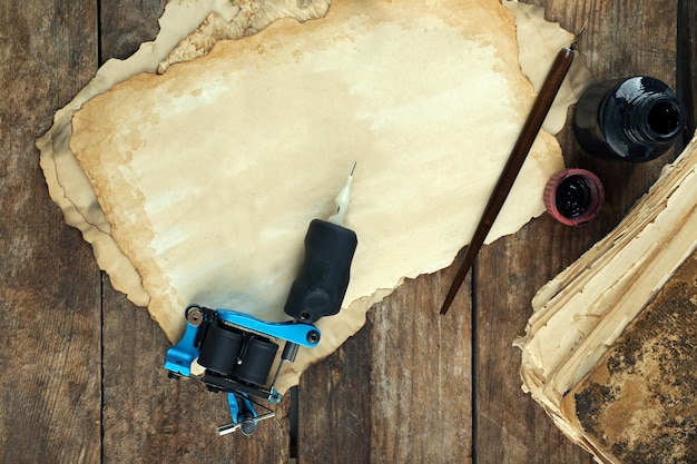 Maschine zum Tätowieren mit altem Papier und Tintenflasche auf dem Tisch aus nächster Nähe