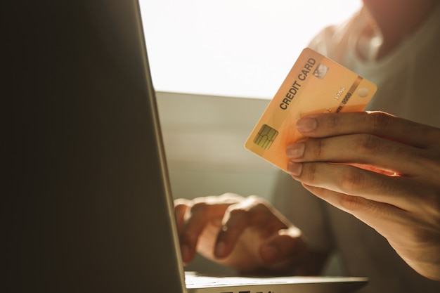 Masculinas mãos segurando um cartão de crédito e usando o computador portátil