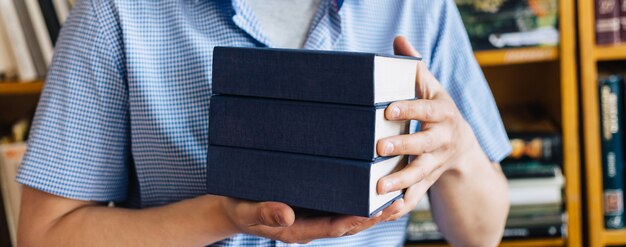 Masculinas mãos segurando uma pilha de livros.