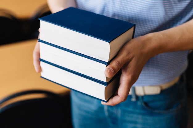 Masculinas mãos segurando uma pilha de livros.