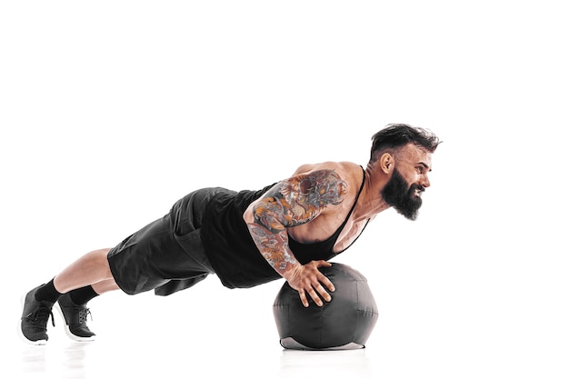 Masculino barbudo tatuado muscular que ejercita pesas de fitness Ejercicios de flexiones de pelota medicinal