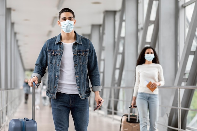 Masculino e feminino usando máscaras enquanto caminhava com bagagem no aeroporto