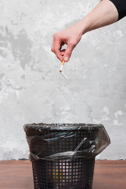 Masculino mão jogando cigarro quebrado para o caixote do lixo