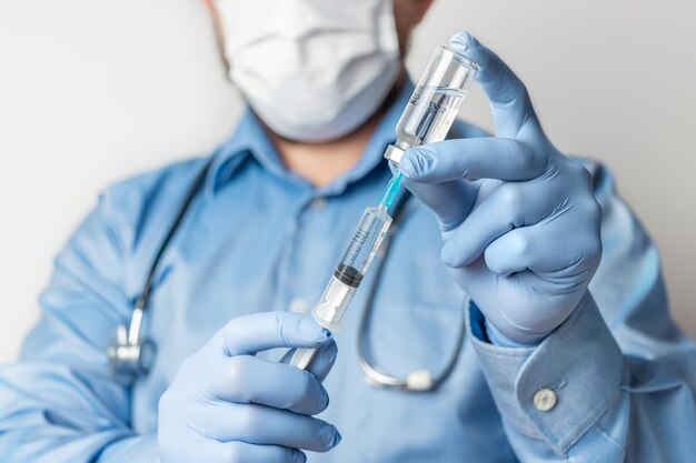 Masculino, médico de camisa azul e luvas, segurando na mão uma seringa e um frasco de vacina contra a doença coronavírus ou gripe, conceito de vacinação.