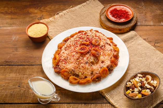 Masfouf de cuscús con frutos secos en un plato sobre una mesa de madera junto a sémola de azafrán y cuscús