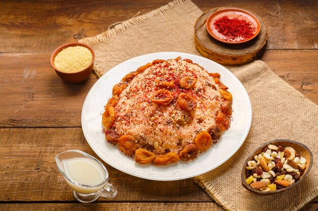 Masfouf de cuscús con frutos secos en un plato sobre una mesa de madera junto a sémola de azafrán y cuscús