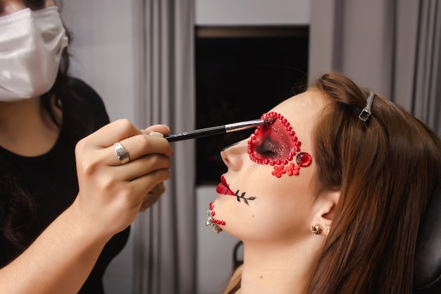 Maskenbildner, der Glitzer auf den Augenlidern eines jungen Mädchens hinzufügt, Tag der Toten Make-up.