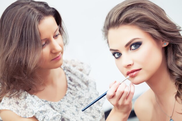 Foto maskenbildner, der lippenstift mit einem pinsel auf die lippen des models aufträgt