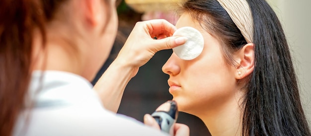 Maskenbildner, der professionelles Make-up auf dem Gesicht einer jungen Frau mit einer Airbrush macht.