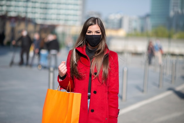 Maskierte Frau, die Einkaufstaschen trägt, während sie ein Masken-Covid- und Coronavirus-Konzept trägt