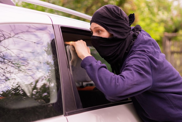 Maskierter Dieb entriegeln und öffnen Sie das Autofenster, um Eigentum zu stehlen