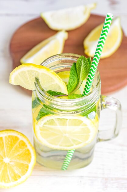 Foto mason-glas aus hausgemachter limonade mit zitronen, minze und grünem papier, stroh auf holz, rustikal