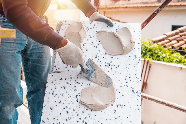 Mason trägt auf einer Baustelle Klebstoff auf eine thermische Verkleidung auf