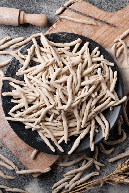 Massa apúlia crua de trigo integral Pizzarieddi ou maccaruni em um prato na mesa preta com farinha. Prato típico de maccheroni fresco de Puglia Salento Itália. Fundo de massa caseira italiana, vista superior