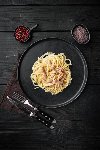 Massa carbonara. conjunto de espaguete com pancetta, ovo e queijo parmesão, mesa de madeira preta, vista de cima plana