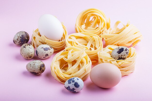 Massa cru crua dos tagliatelle com ovos de codorniz em um rosa pastel.