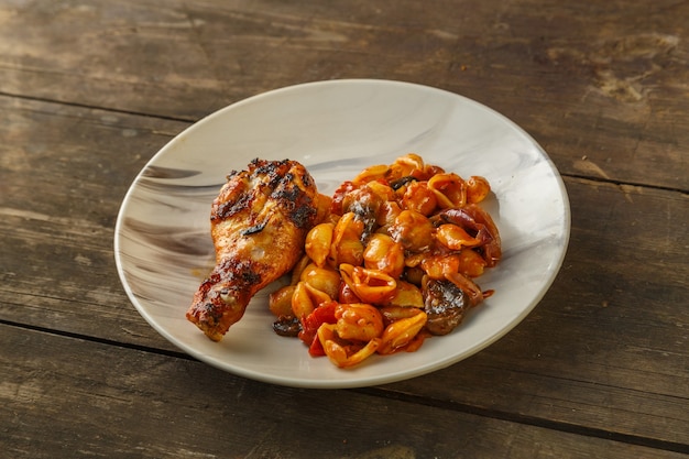 Massa de concha no tomate com coxa de frango assada na grelha em uma mesa de madeira.