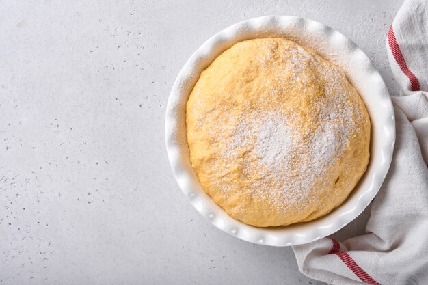 Massa de fermento cru com abóbora em uma tigela branca coberta com uma toalha na mesa da cozinha enfarinhada, ideia de receita. Conceito casa assando pão, pãezinhos ou cinnabon ou fazendo massa.