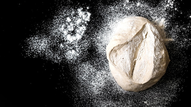 Foto massa de pão crua polvilhada com farinha branca em fundo preto