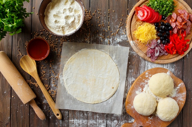 Massa de pizza com ingredientes na mesa de madeira