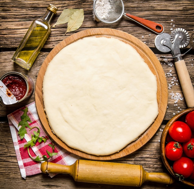 Massa de pizza com tomate e ervas com um rolo.