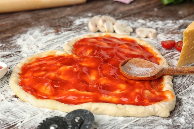 Massa de pizza em forma de coração coberta com molho de tomate na mesa