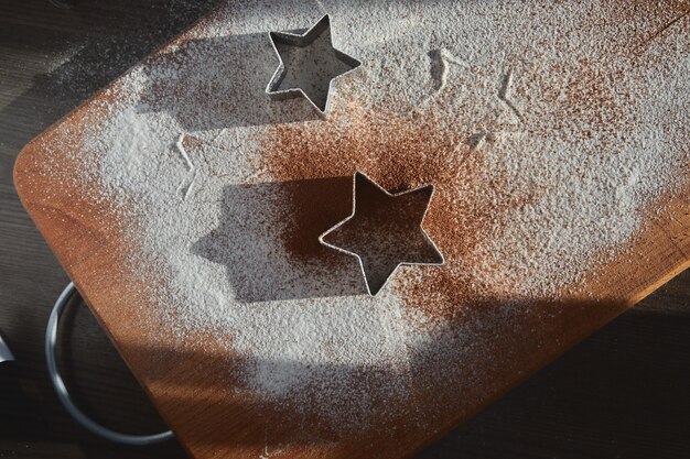 Massa de shortbread para biscoitos de gengibre enrolada na placa de madeira. cortando biscoitos em forma de estrela. conceito de ano novo e processo de cozimento. cookies na mesa de madeira marrom escura. fazendo família