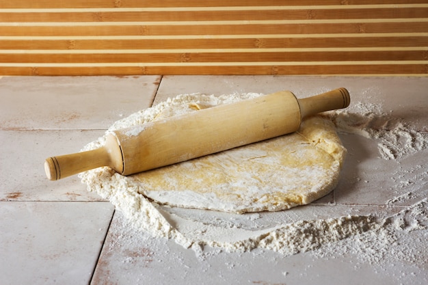 Massa é rolada sobre a mesa. perto está um rolo. a mesa é polvilhada com farinha.