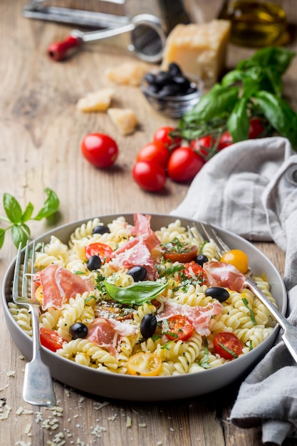 Massa espiral de fusilli italiana com tomate uva, azeitonas, presunto e queijo parmesão em um prato