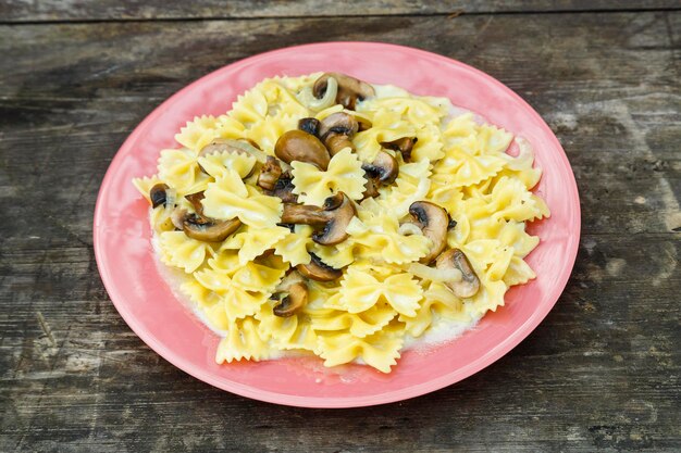 Massa farfalle em molho cremoso com cogumelos em um prato grande sobre uma mesa de madeira escura