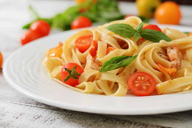 Massa Fettuccine em molho de tomate com frango, tomates decorados com manjericão sobre uma mesa de madeira