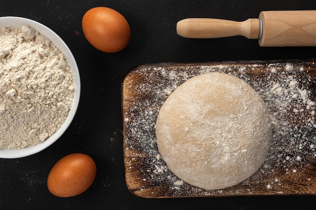 Massa fresca crua para pão ou pizza com ovos no escuro com polvilhada de farinha.